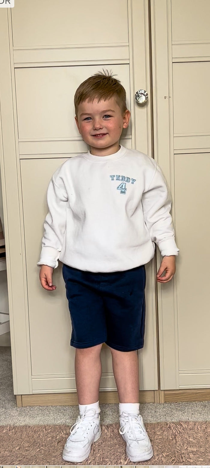 Little boy wearing white birthday jumper in varsity style embroidery