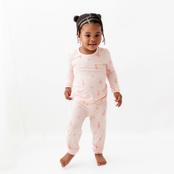 A toddler in a pink ballerina-print pajama set with long sleeves and matching pants.