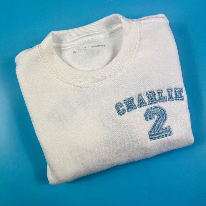 White birthday jumper with child’s name and age embroidered in baby blue