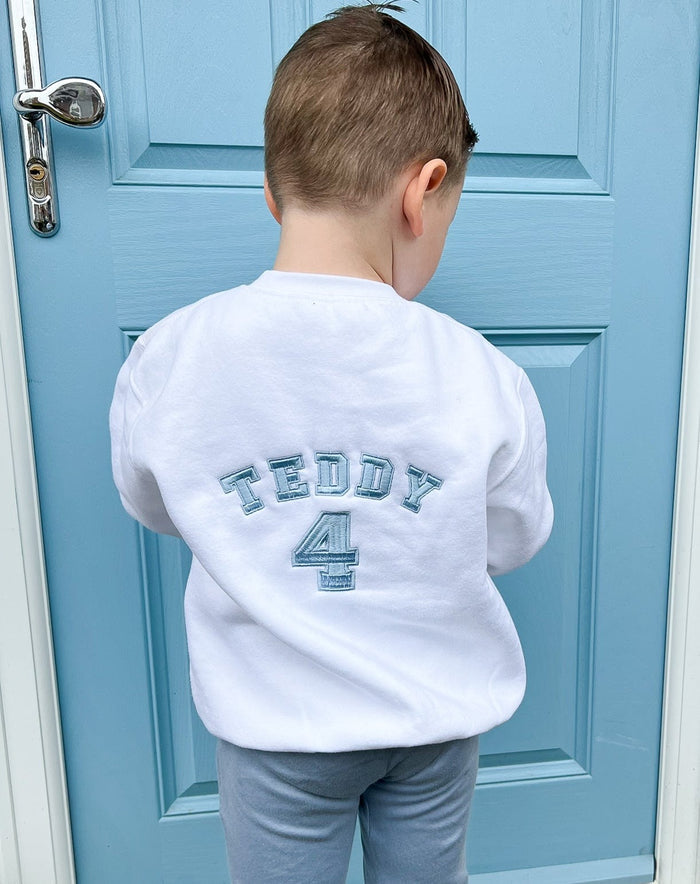 Boy wearing a white jumper with his name and age embroidered on the back