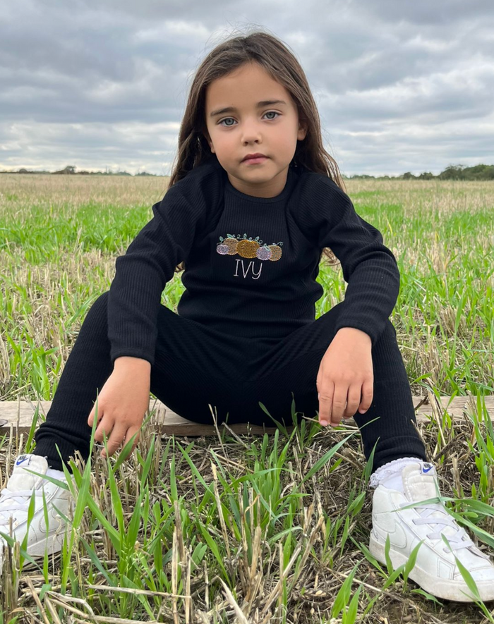 girl wearing black loungewear with pink and orange pumpkin design and childs name in pink
