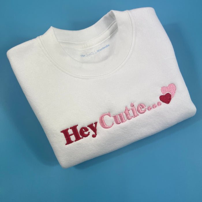 White sweatshirt with hey cutie embroidered on the front in pink and red