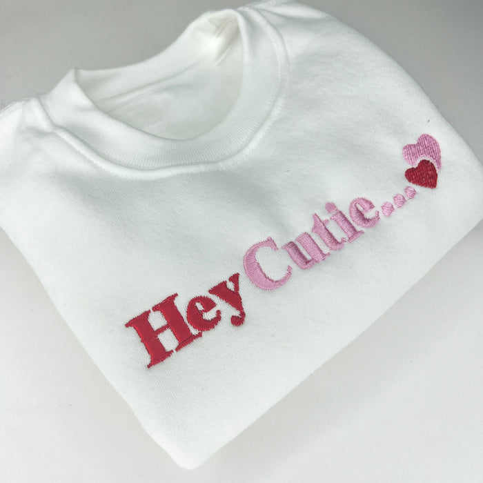White sweatshirt with hey cutie embroidered on the front in pink and red