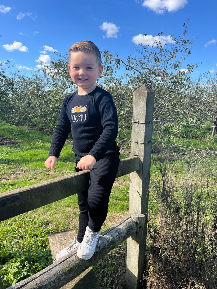 young bou sitting on fence in black loungewear with pumpkin design in blue and orange