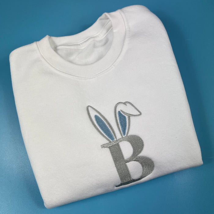 Folded white sweatshirt with Bunny ears on th letter B on a blue background