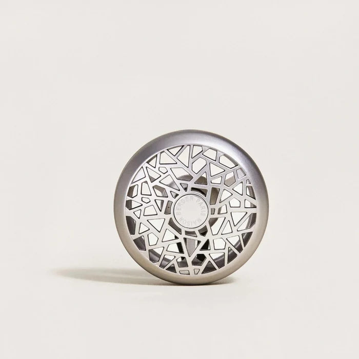 A round metallic silver car diffuser with an intricate geometric cutout pattern.