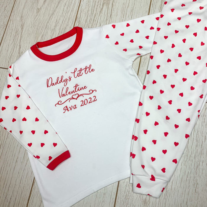 Children's Valentine's Day pyjamas with a white base and red hearts, featuring text on the front.