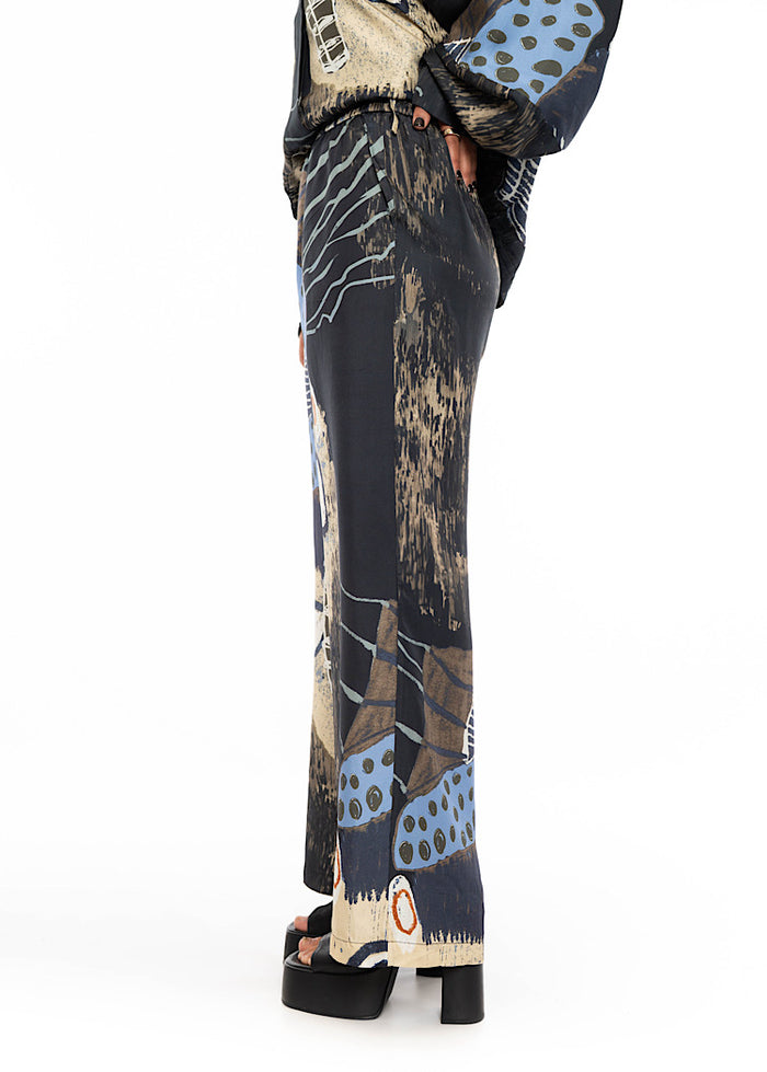 A close up of a model wearing a wide leg Silk trousers. Standing at a side angle; drawing attention to the trouser length.
