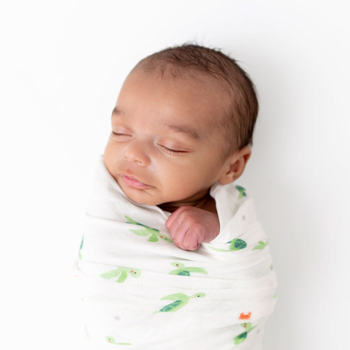 Newborn baby swaddled in a white blanket with green turtle patterns on a white background
