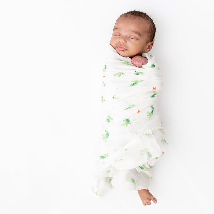 Newborn baby wrapped in a white swaddle with green and orange patterns on a white background